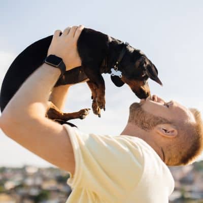 Man in yellow shirt holding up dog kissing
