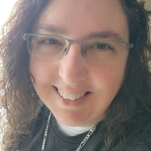 Smiling pet sitter with curly hair and glasses, wearing a casual shirt and chain necklace